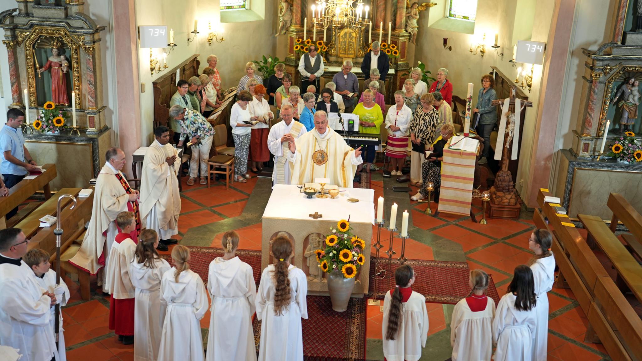Weihbischof Peters, ein Chor sowie Messdienerinnen und Messdiener feiern Gottesdienst in der Kirche in Faid.
